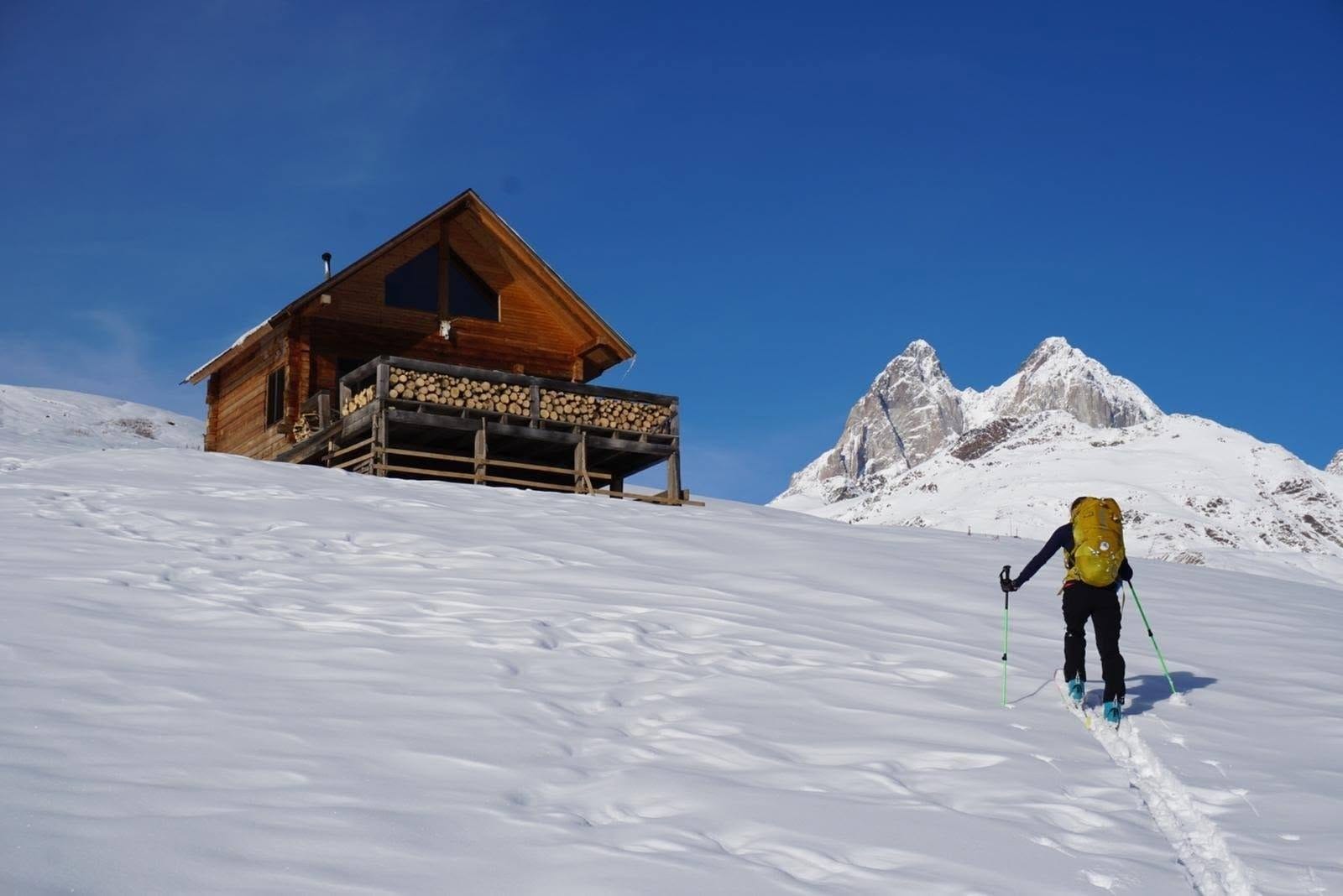 Cloudbase Hut with Ushba behind and a skier skinning up the snowy slope