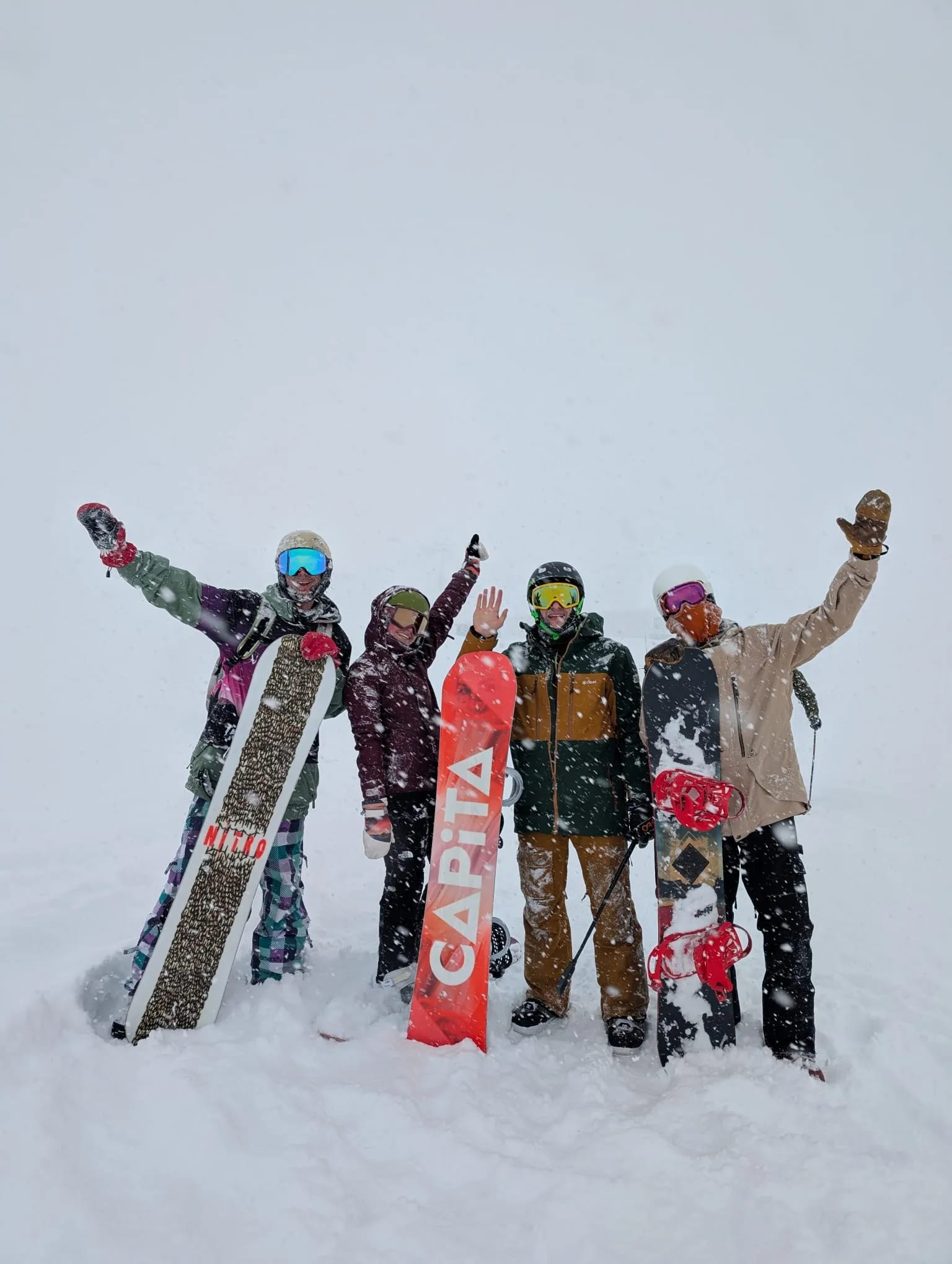 Four riders with snowboards waving in falling snow in Gudauri