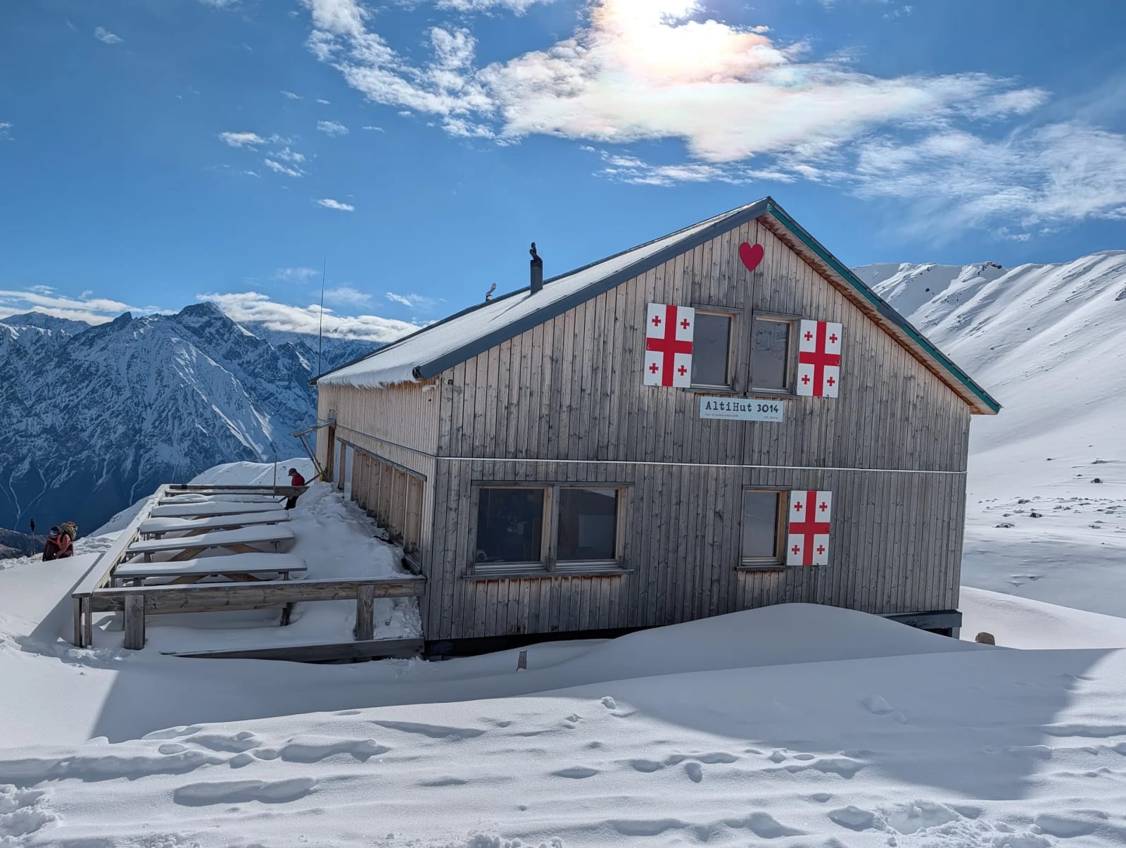 Mountain hut on a snowy slope below a broad mountain ridge