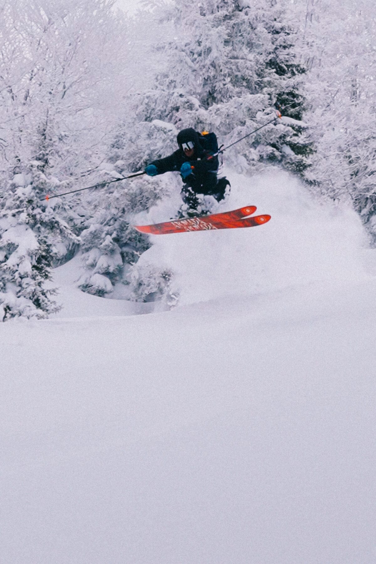 A skier launching through snow-covered trees in deep powder